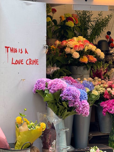 In a flower shop, a variety of fresh floral arrangements are displayed in metal and plastic buckets, featuring hydrangeas in shades of pink, purple, and blue, along with roses in soft pink and white. 